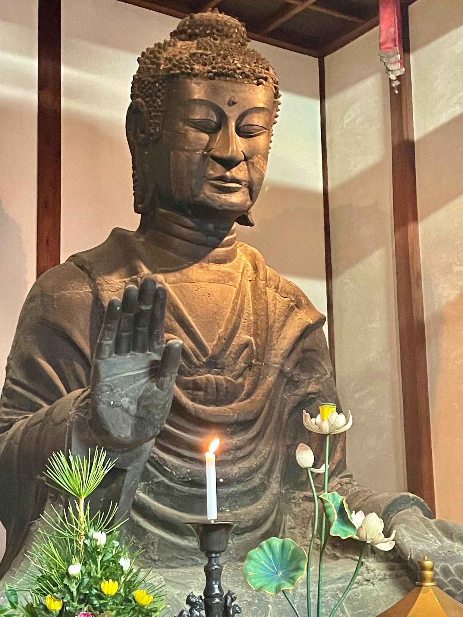 灯明と花を前に穏やかな表情で坐す仏像